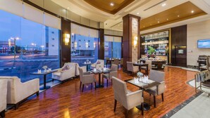 Un vestíbulo de hotel con área de bar, zonas de estar y ventanas grandes que dan a la calle.