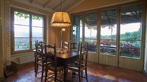 A dining area with a wooden table and chairs, large windows with views of greenery, and a hanging lamp. - Agriturismo Monteverde (Castelnuovo Magra)
