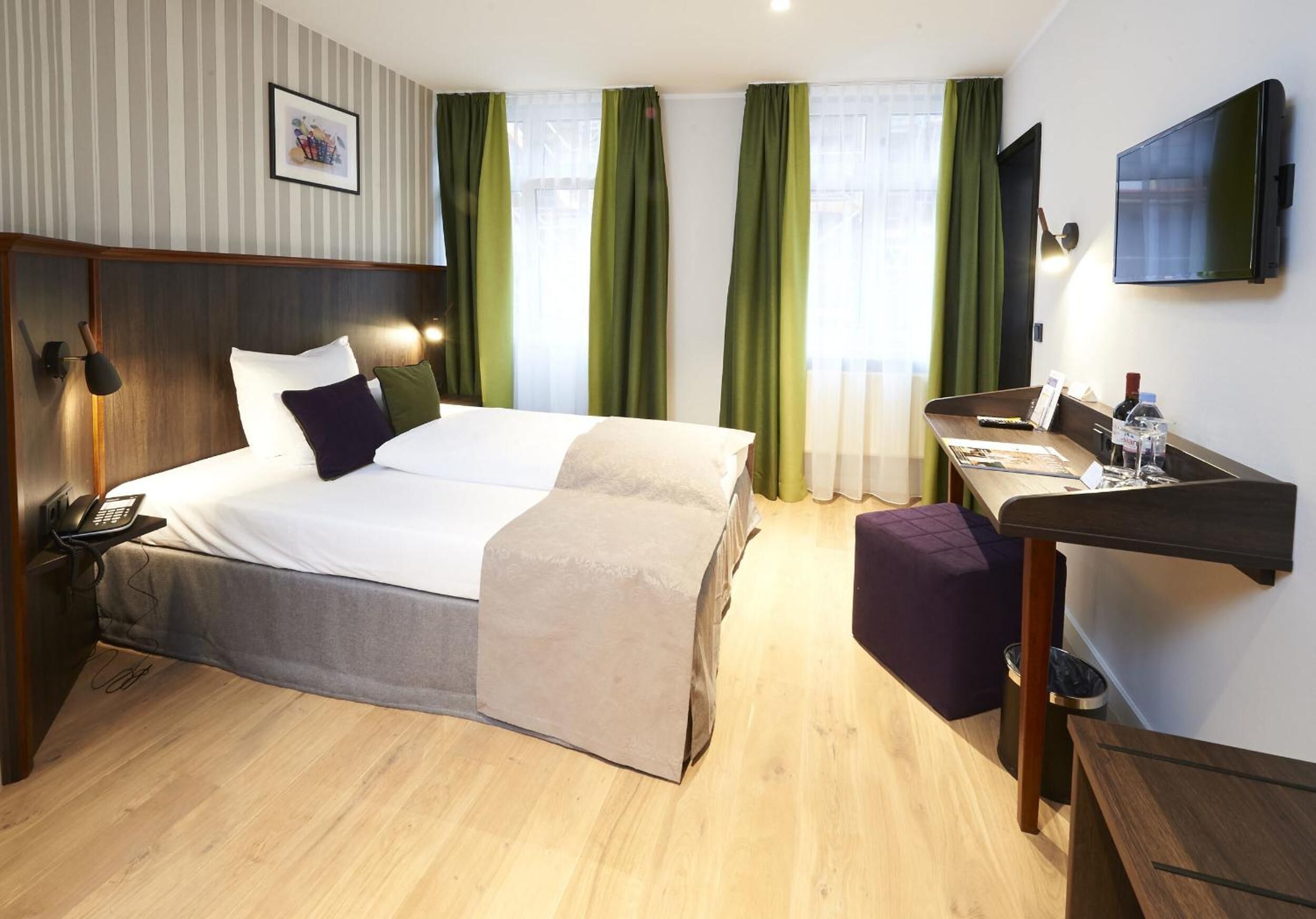 A hotel room with a bed, bedside table, desk, and a TV.