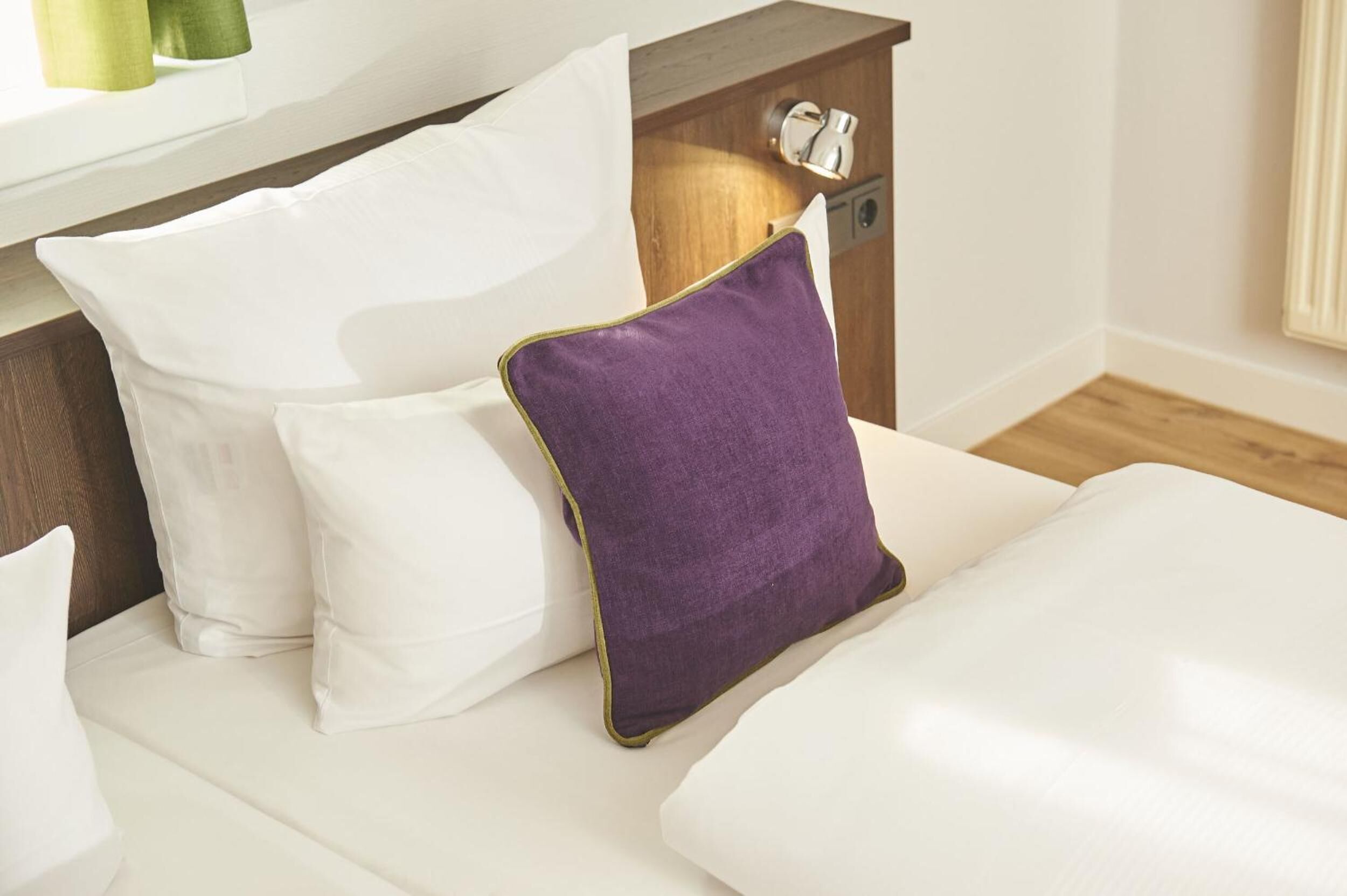 A bed with white bedding and a purple pillow.