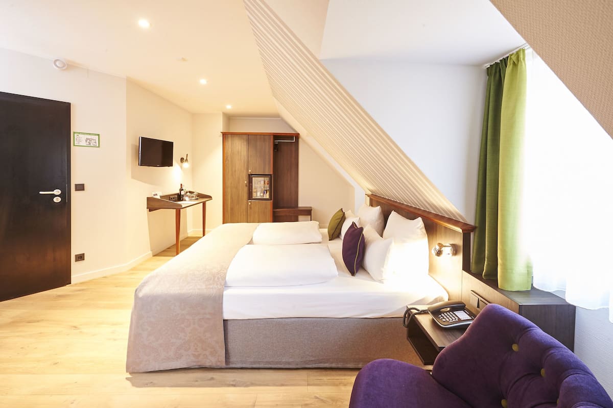 Quarto de hotel com uma cama grande, uma escrivaninha com telefone e uma TV na parede.