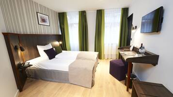 A hotel room with a bed, bedside table with a phone, a desk with a chair, a TV, and a window with curtains.