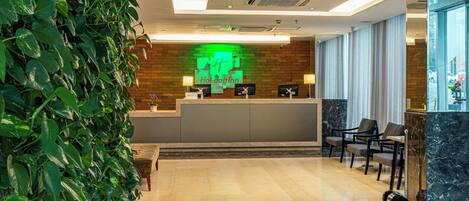 A hotel reception area with a brick wall, a reception desk, and a seating area with chairs.
