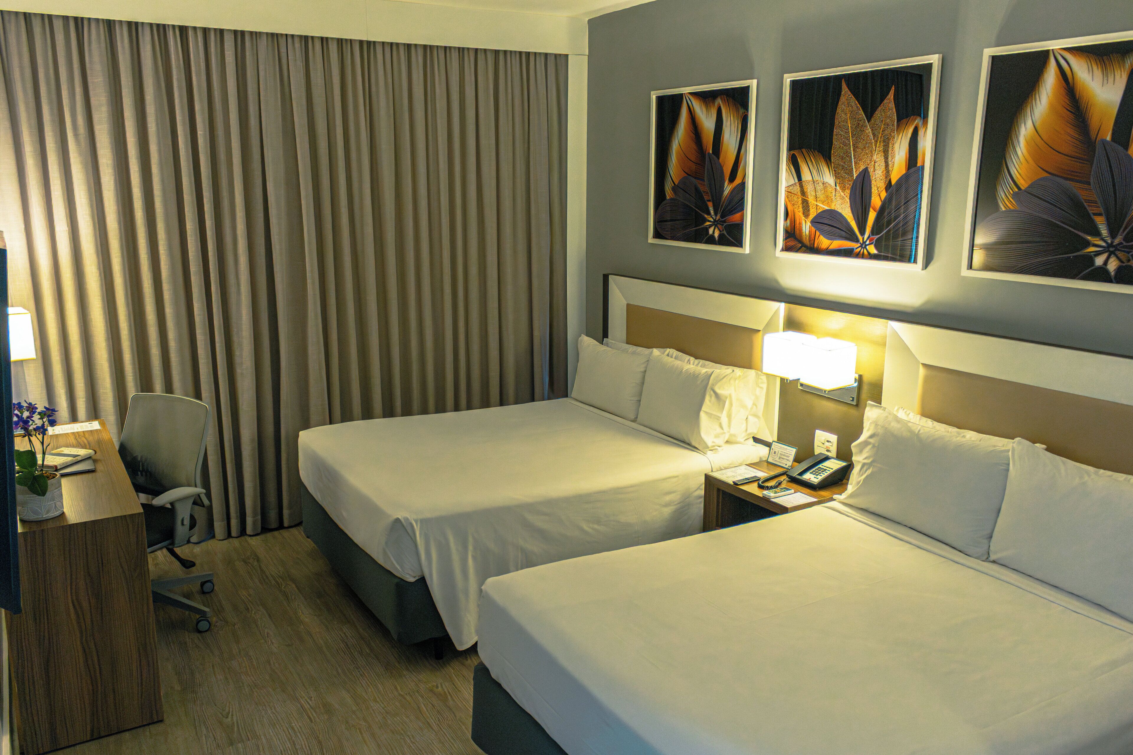 A hotel room with two beds, a desk with a chair, a telephone, and artwork on the wall.