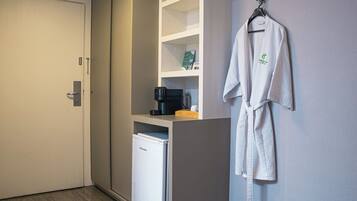 A hotel room with a wardrobe, a minibar, a coffee machine, and a robe hanging on the wall.