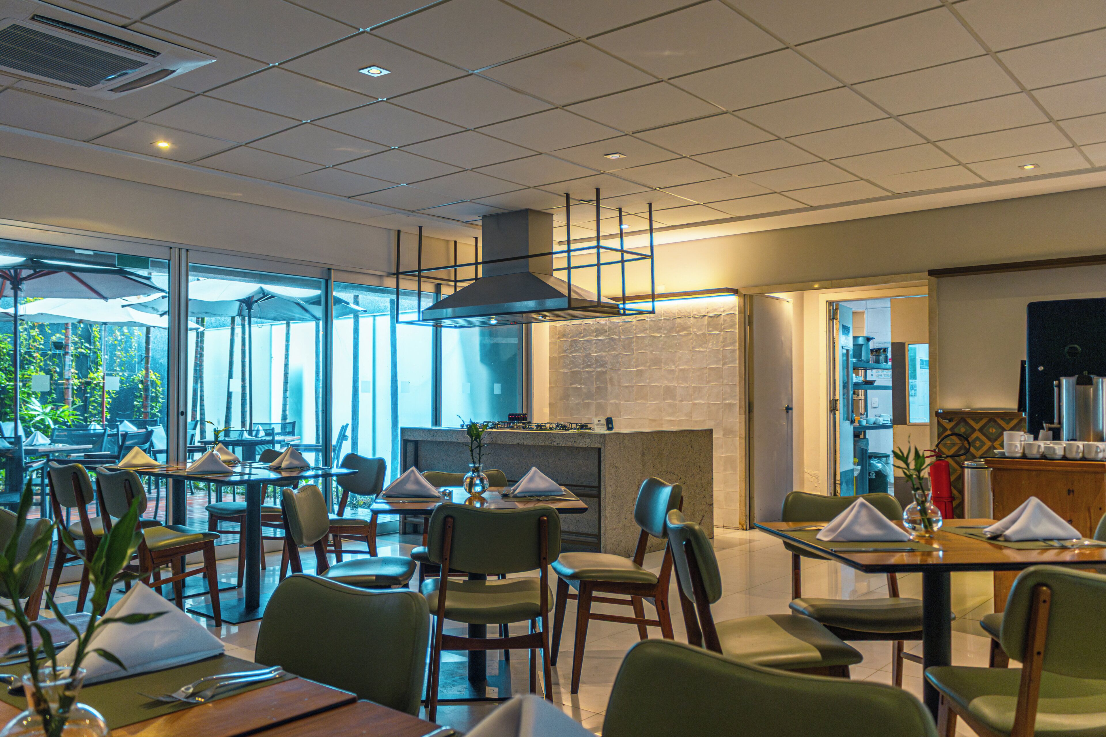 Restaurante com mesas internas, parede de tijolos e vista através de grandes janelas.