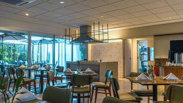 Restaurante com mesas internas, parede de tijolos e vista através de grandes janelas.