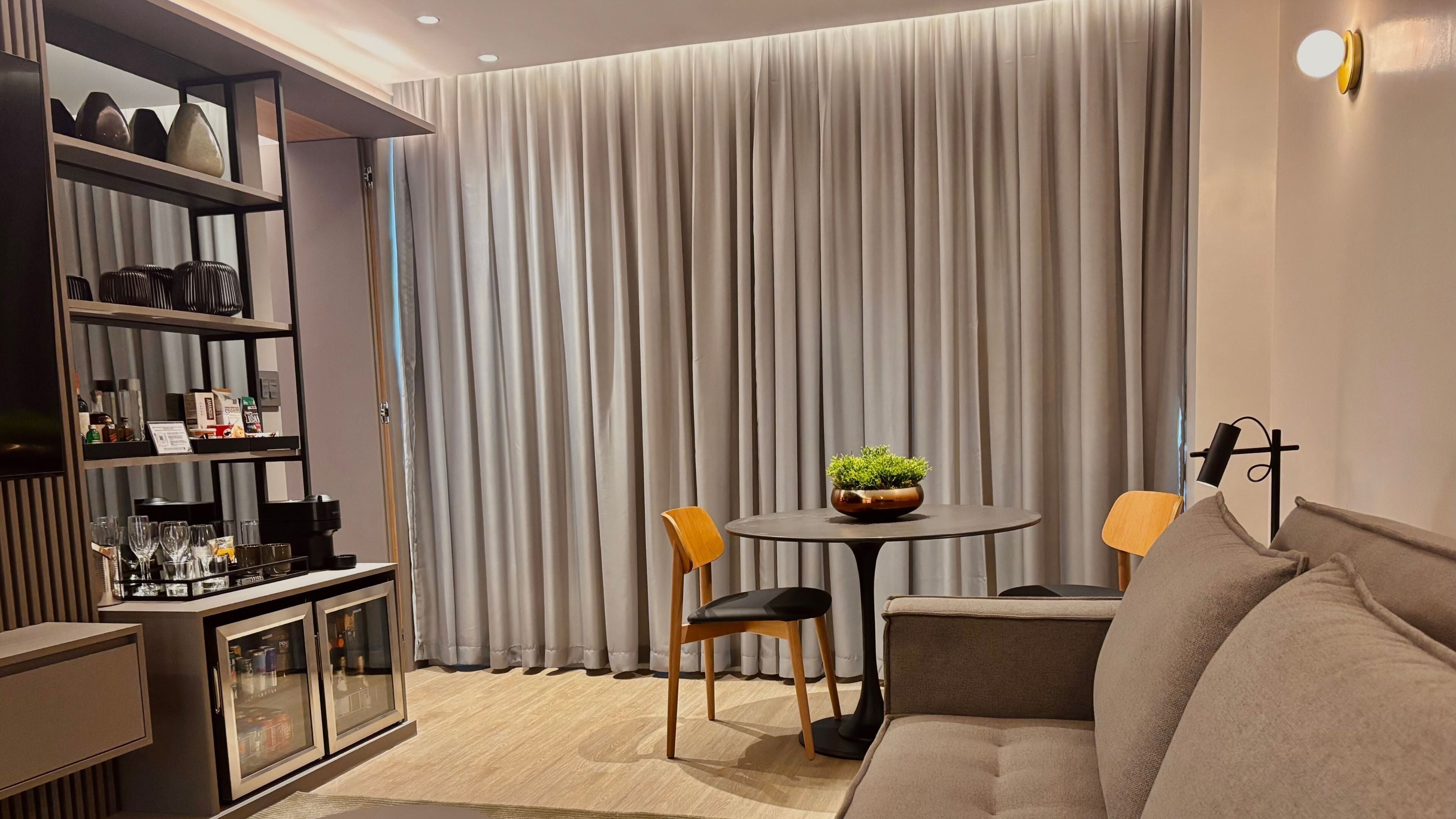A modern living room with a sofa, a dining table with chairs, a coffee machine, and a bookshelf.