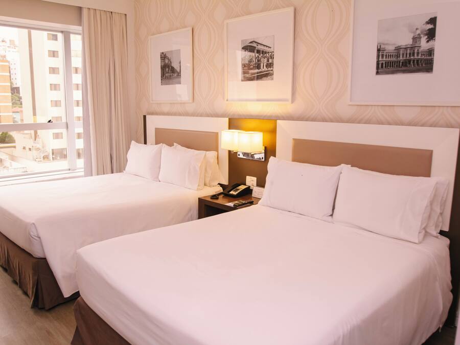 A hotel room with two beds, a nightstand with a lamp, and framed pictures on the wall.