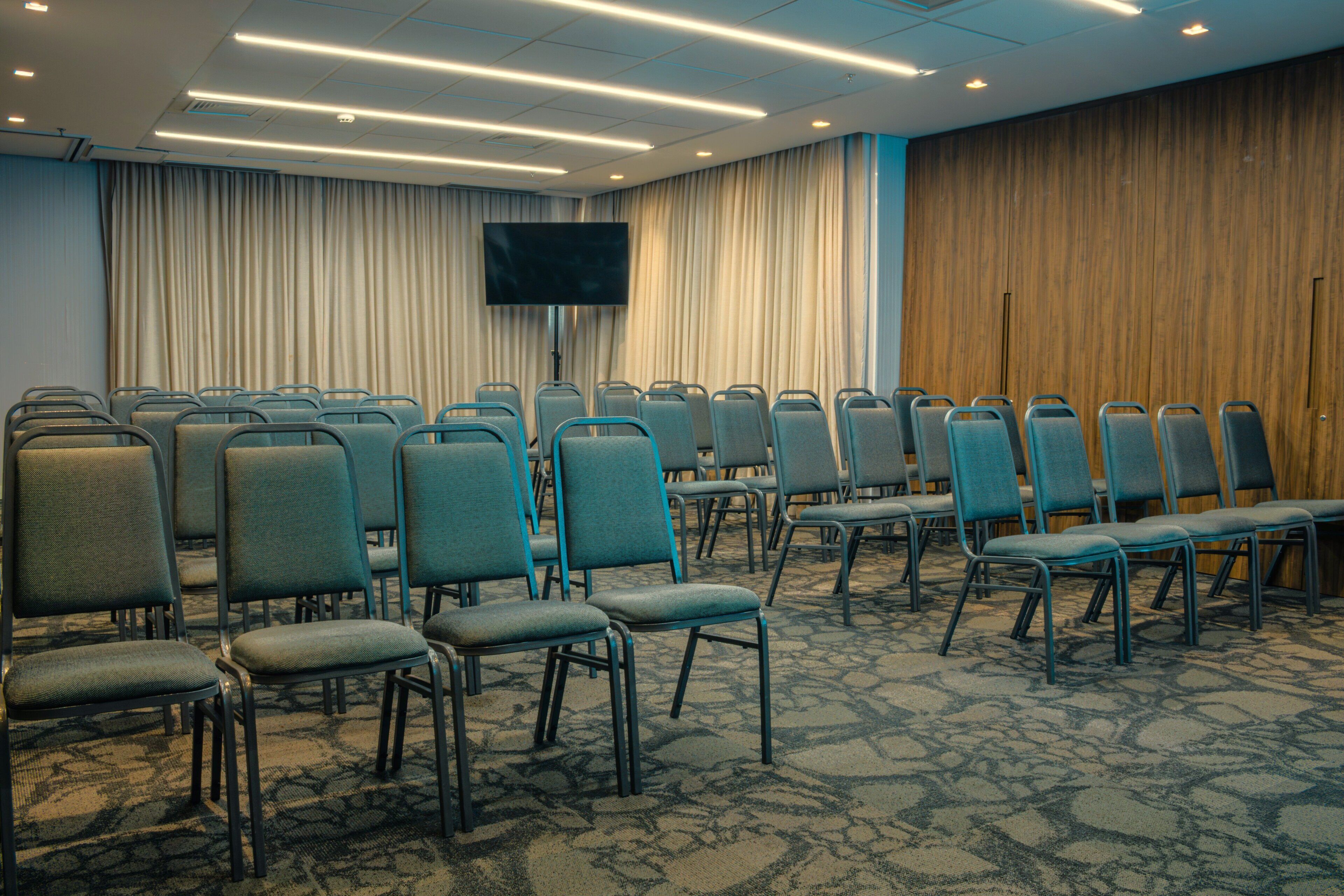 Un salón de conferencias con filas de sillas, un televisor de pantalla plana grande y una alfombra estampada.