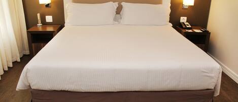 A hotel room with a large bed, two bedside tables, a nightstand, a lamp, and a telephone.