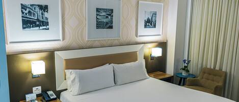 Ett hotellrum med en säng, två sängbord, en stol och tre inramade tavlor på väggen.