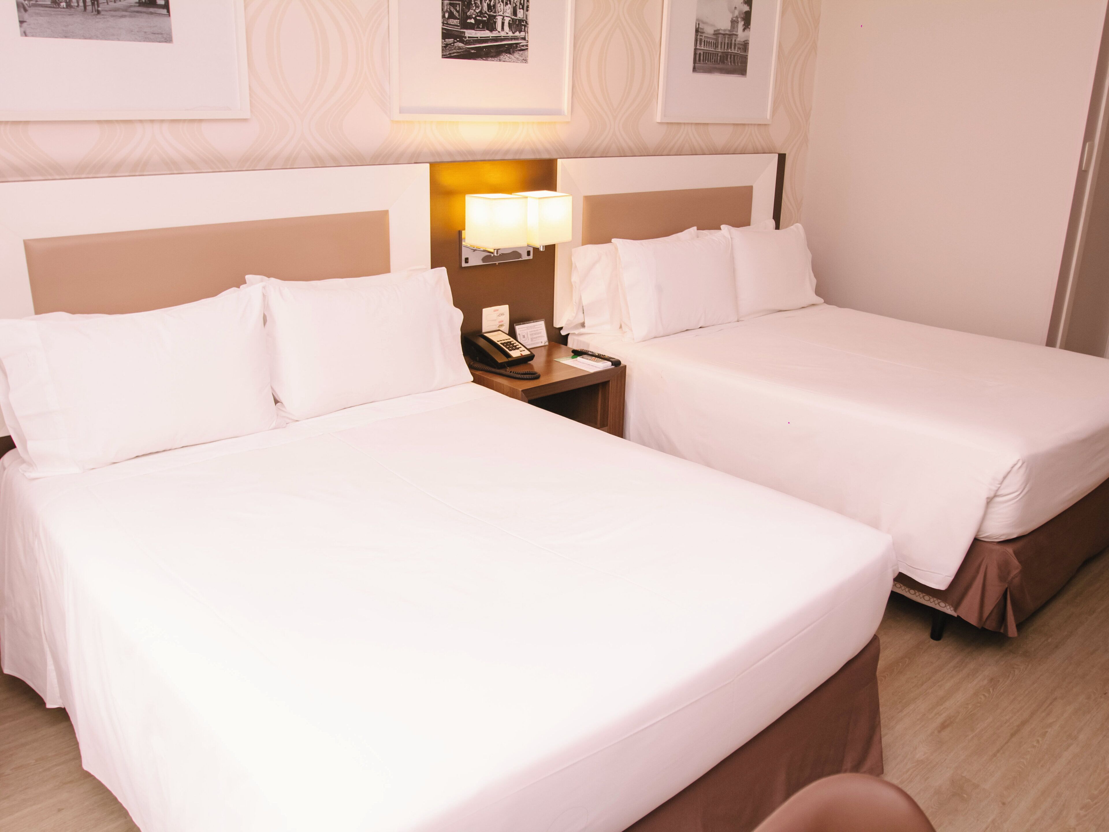 A hotel room with two beds, a nightstand with a lamp, and framed pictures on the wall.