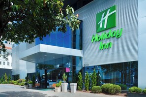A modern building with a large glass facade, a prominent green logo, and the name 'Holiday Inn' displayed on the side. - Holiday Inn Belo Horizonte Savassi by IHG (Belo Horizonte)