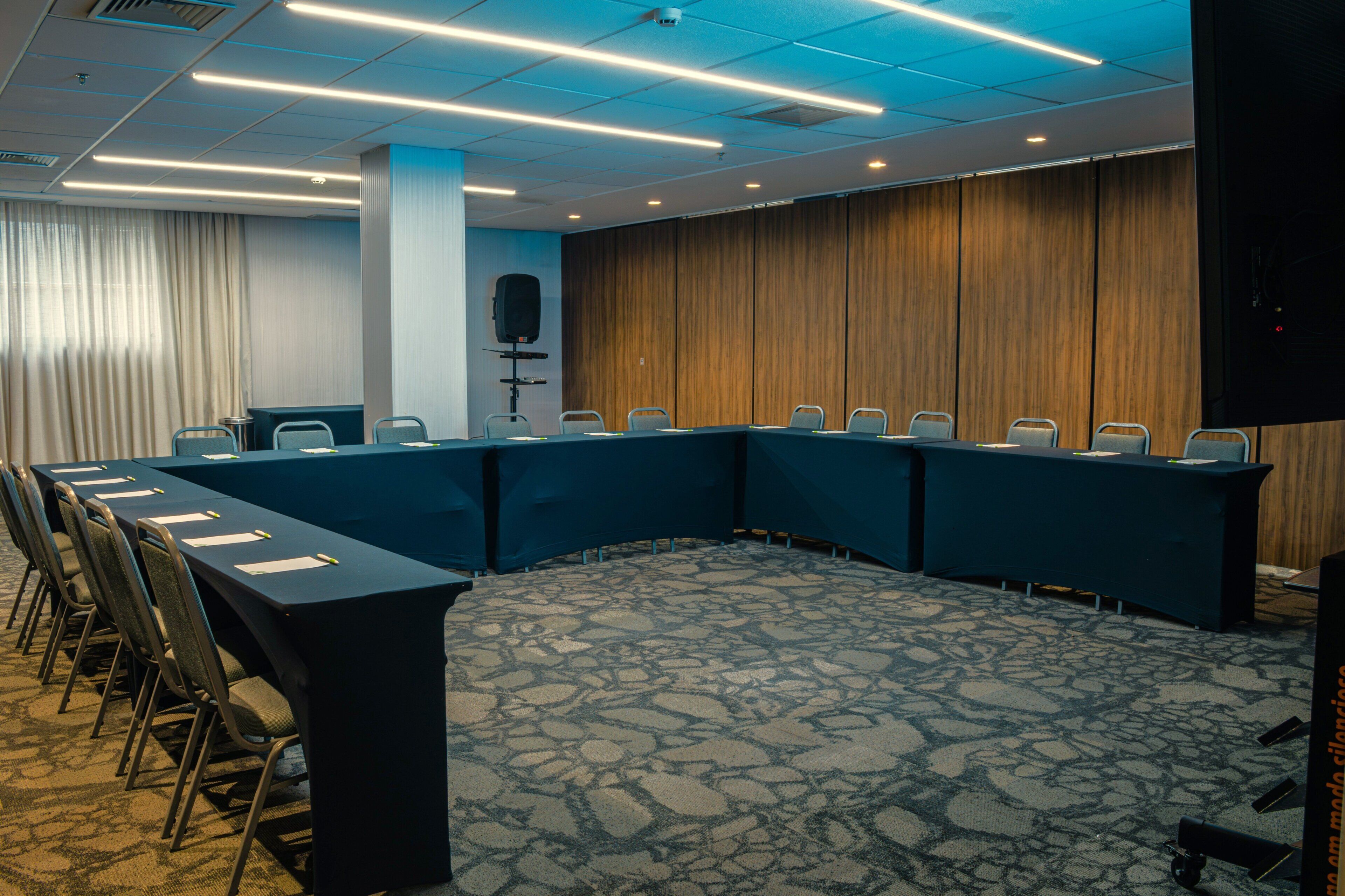 Un salón de conferencias con una larga mesa, sillas, un atril y un sistema de sonido.