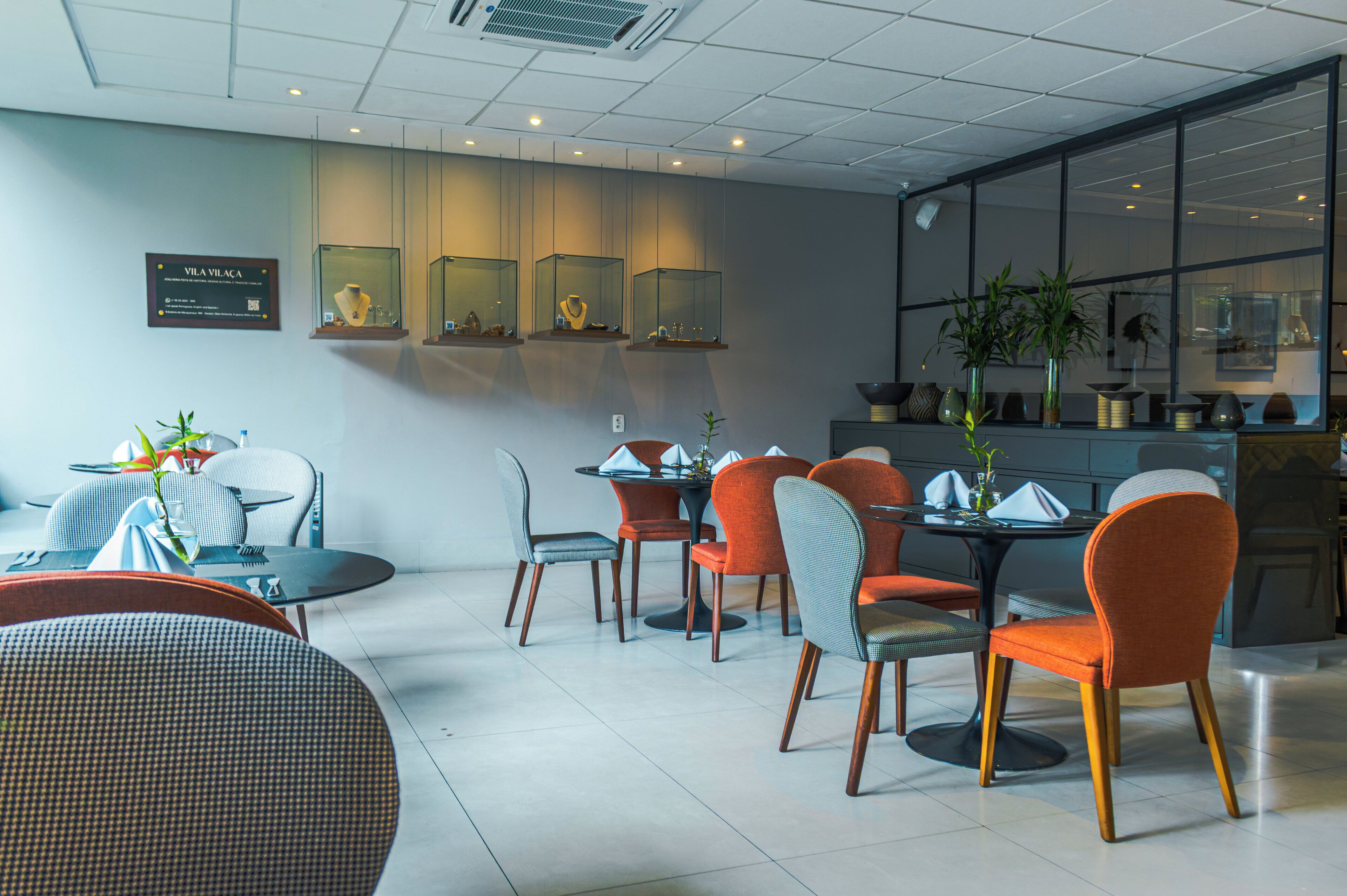 Un espace repas moderne avec des tables et des chaises rondes, une grande fenêtre offrant une belle vue et une vitrine où sont exposés des bijoux.