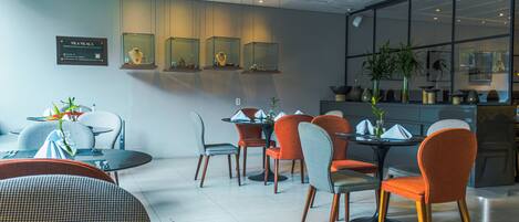 Un espace repas moderne avec des tables et des chaises rondes, une grande fenêtre offrant une belle vue et une vitrine où sont exposés des bijoux.