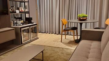 Una sala de estar moderna con un sofá, una mesa de comedor con sillas, un aparador con puertas de cristal y una planta en maceta.