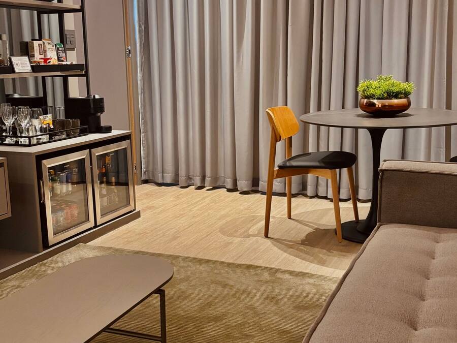 Una sala de estar moderna con un sofá, una mesa de comedor con sillas, un aparador con puertas de cristal y una planta en maceta.