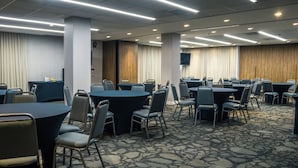 A conference room with multiple tables and chairs, a carpeted floor, and a flat-screen TV mounted on the wall.