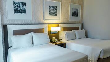 A hotel room with two beds, a nightstand with a lamp, and three framed pictures on the wall.