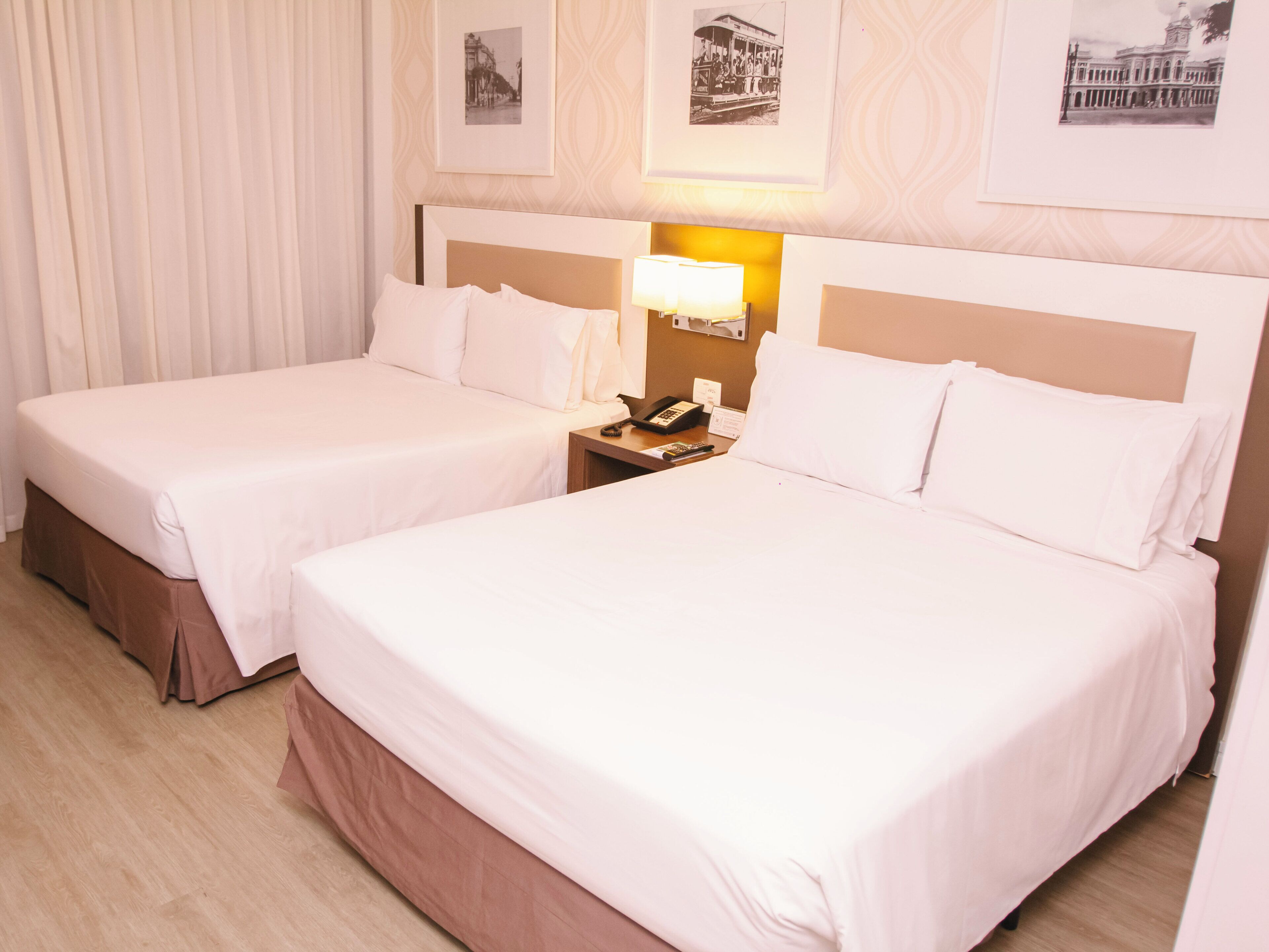 A hotel room with two beds, a nightstand with a lamp, and framed pictures on the wall.