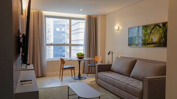 A modern living room with a sofa, a coffee table, a dining table with chairs, a TV, and a painting on the wall.