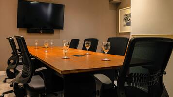 A conference room with a long table, six chairs, a flat-screen TV, and a framed picture on the wall.