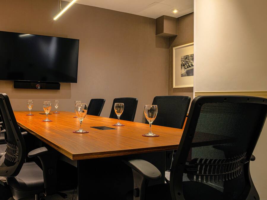A conference room with a long table, six chairs, a flat-screen TV, and a framed picture on the wall.