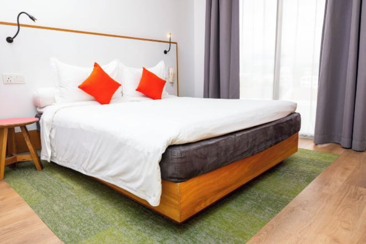 Ett modernt hotellrum med en sängram i trä, vita sängkläder och en grön matta.