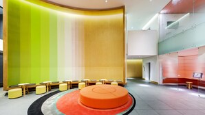 Un vestíbulo moderno con una zona de estar circular naranja, una pared verde y amarilla, y un separador de vidrio.
