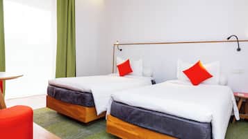 A hotel room with two beds, each with white bedding and red pillows, a wooden headboard, and a green carpet.