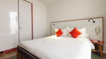 Quarto de hotel moderno com uma cama grande, mesa de cabeceira de madeira, telefone e guarda-roupa.