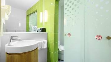 Un baño con lavamanos blanco, azulejos verdes y una puerta de cristal con un cartel de 'deslizar'.