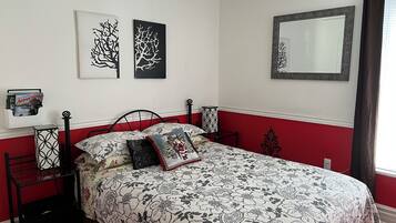Un dormitorio con cama, mesita de noche, espejo y decoración en la pared.