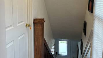 A hallway with a white door marked with the number 2, a wooden column, a black and white patterned mat, and a staircase leading to a room with a window.