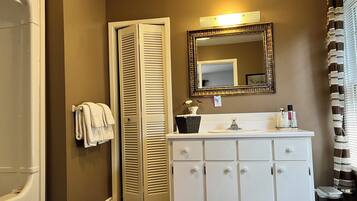 A bathroom with a white vanity, a mirror, a towel rack, and a shower area.