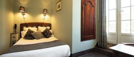 A neatly made bed with a wooden headboard, two bedside lamps, a bedside phone, and a window with curtains.