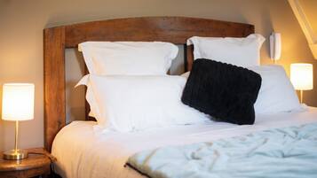Una cama bien tendida con sábanas blancas y un cojín negro, flanqueada por dos lámparas de noche en mesitas de madera.