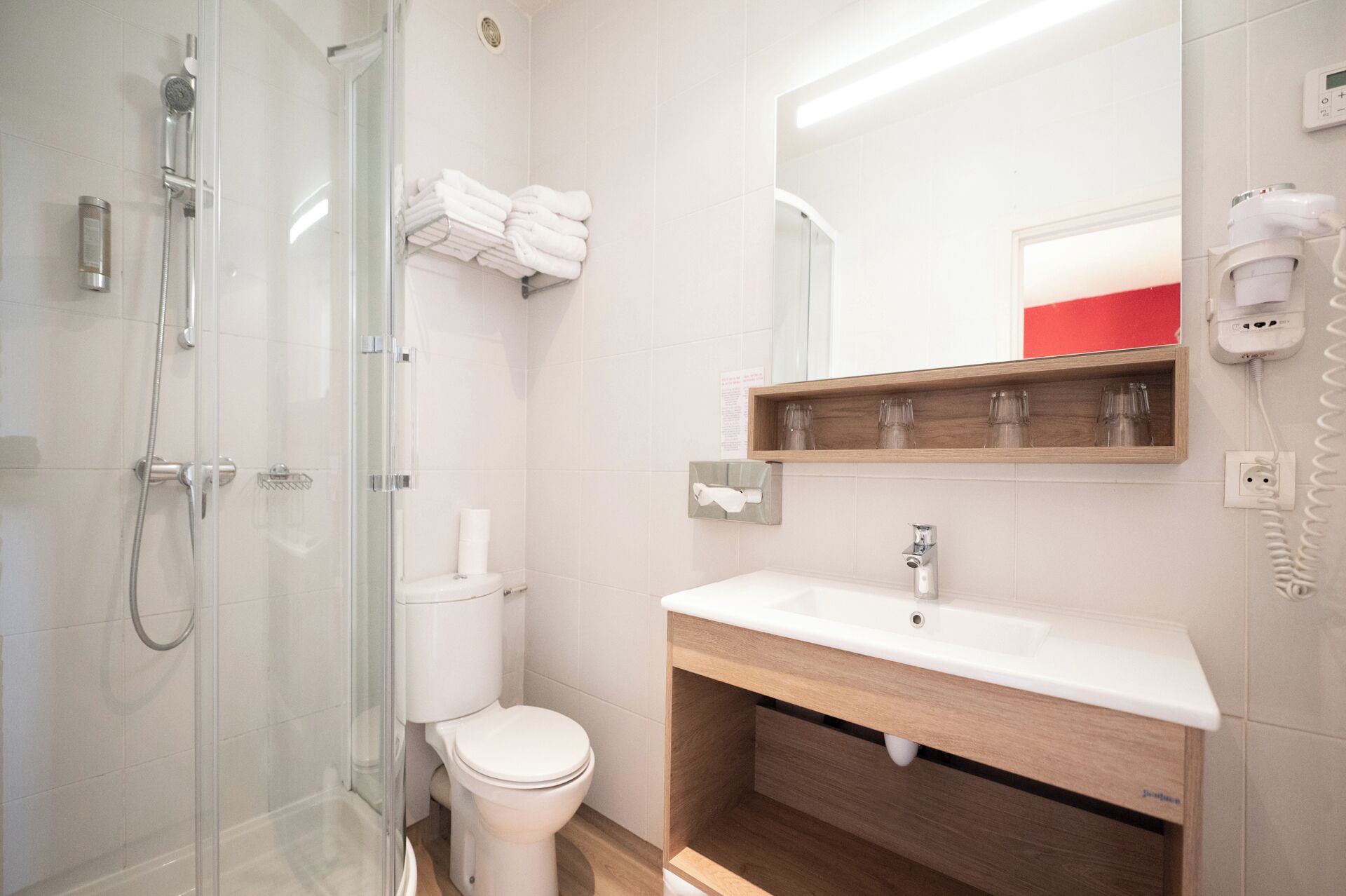 A modern bathroom with a glass shower enclosure, a toilet, a sink with a wooden vanity, and a mirror above the sink.