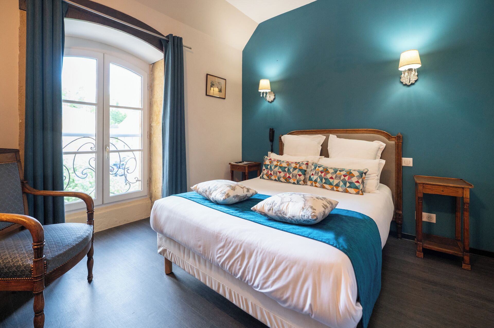 Une chambre à coucher avec un grand lit, deux lampes de chevet, une chaise et une fenêtre avec des rideaux.