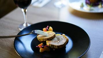 Un plato de comida con un tenedor sobre un plato oscuro, una copa de vino tinto y una servilleta sobre una mesa.