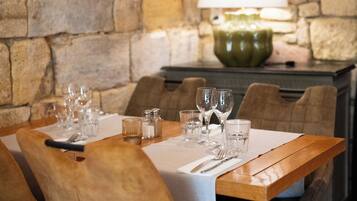 A dining table set with glasses, cutlery, and salt and pepper shakers, with a stone wall and a lamp in the background.