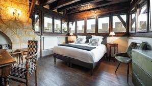 Een slaapkamer met een groot bed, houten balken, stenen muren en uitzicht door ramen.