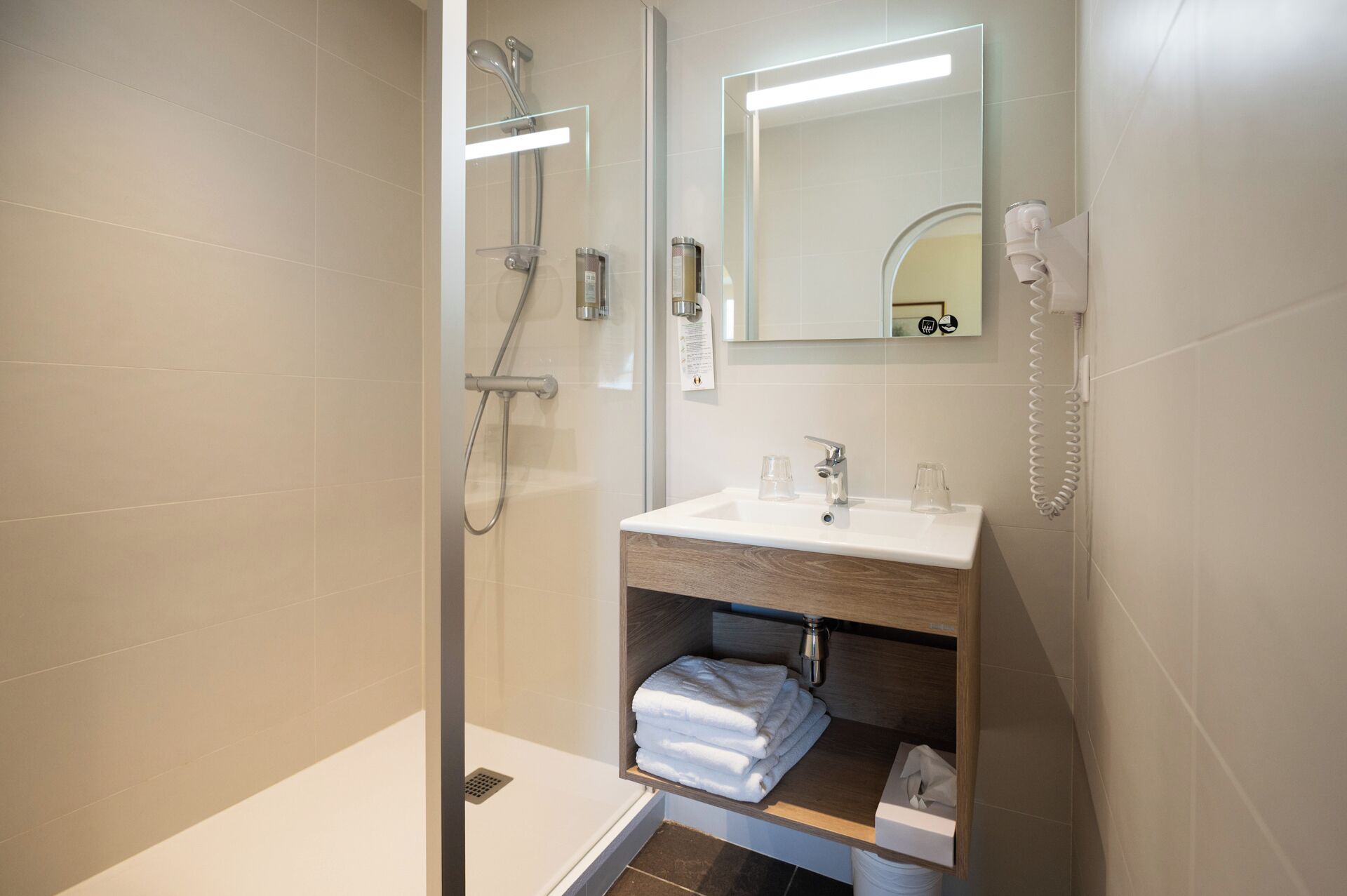 Une salle de bain moderne avec une douche à parois de verre, un lavabo avec un miroir au-dessus et un porte-serviettes avec des serviettes pliées.