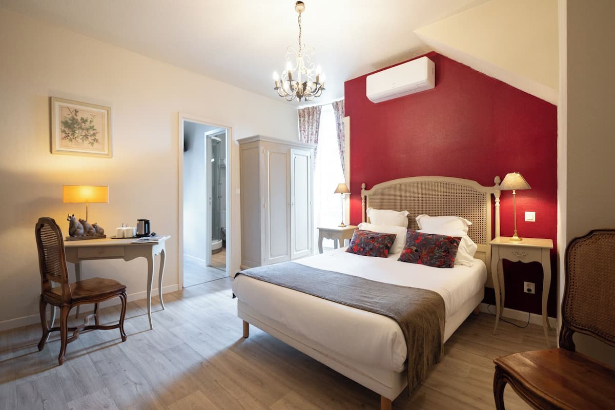 A hotel room with a bed, desk, chair, and a red accent wall.