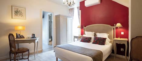 A hotel room with a bed, desk, chair, and a red accent wall.