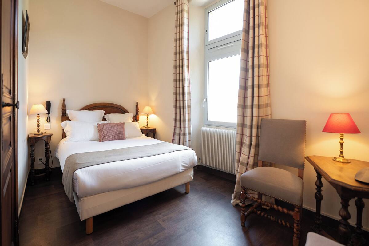 A neatly arranged bedroom with a large bed, two bedside tables with lamps, a chair, and a window with curtains.