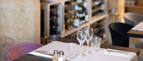 A restaurant interior with a wine rack in the background, a table set with glasses and cutlery, and a pink chair.