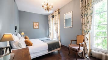 Ein Schlafzimmer mit Bett, Nachttischlampen, einem Sessel, einem Spiegel und einem Fenster mit Vorhängen.